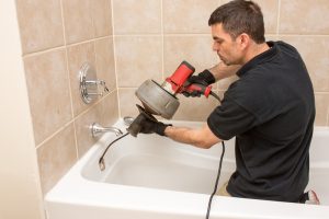 Plumber unclogging a tub drain with an electric auger.