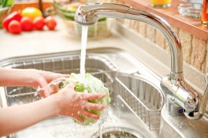person washing lettuce under kitchen sink faucet